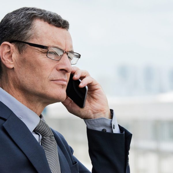 Portrait of serious mature lawyer standing outdoors and calling on pphone