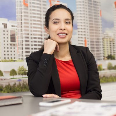 Portrait of cheerful mixed-race woman sitting at desk in real estate office and looking at camera